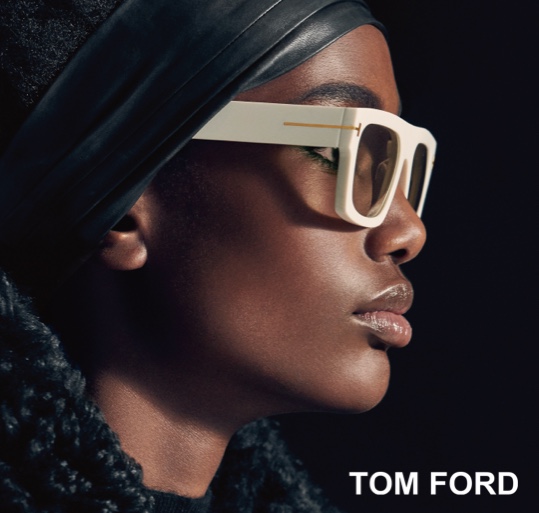 Tom Ford Luxury Eyewear - Webster Eye Doctor | Clear Lake Eye Center A stylish woman wearing bold white Tom Ford sunglasses and a sleek black headscarf poses against a dark background. - Webster Eye Doctor | Clear Lake Eye Center