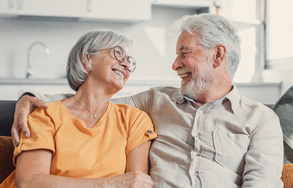 Happy senior couple sitting together at home and smiling at each other, symbolizing comfort, trust, and comprehensive eye care for all stages of life – eye care pearland tx