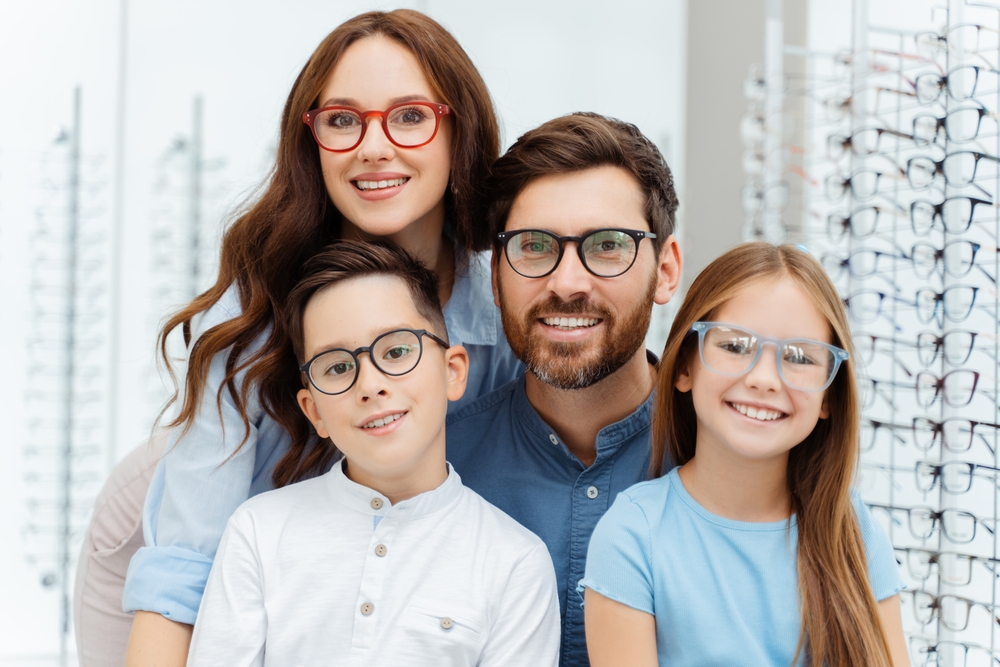 Happy family of four wearing eyeglasses and smiling indoors, symbolizing trusted, family-focused eye care and clear vision for all ages – eye care pearland tx